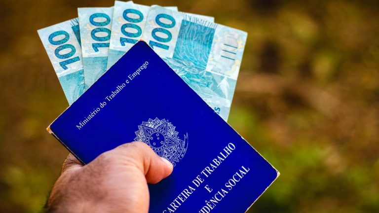 July 28, 2021, Brazil. In this photo illustration the a man displays his Work and Social Security Card in Brazil with three hundred reais bills